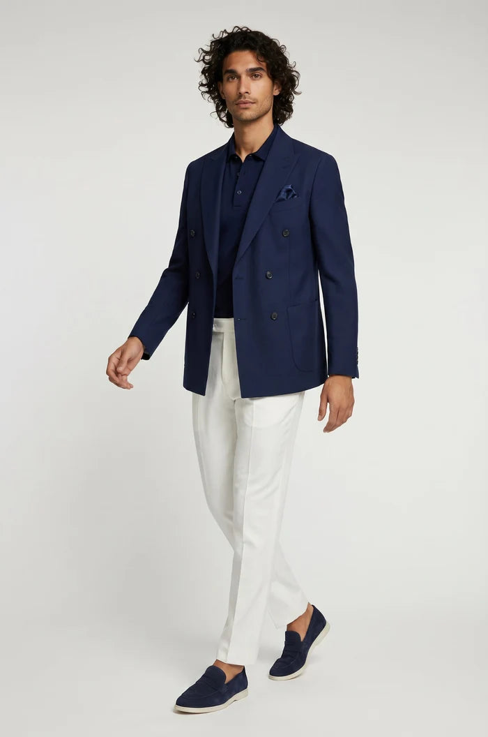 Man wearing a navy blazer, white pants, and navy shoes on a light gray background