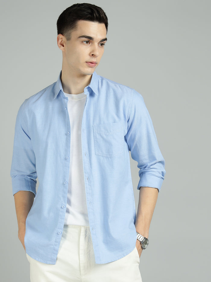 Man wearing a light blue shirt over a white t-shirt on a gray background