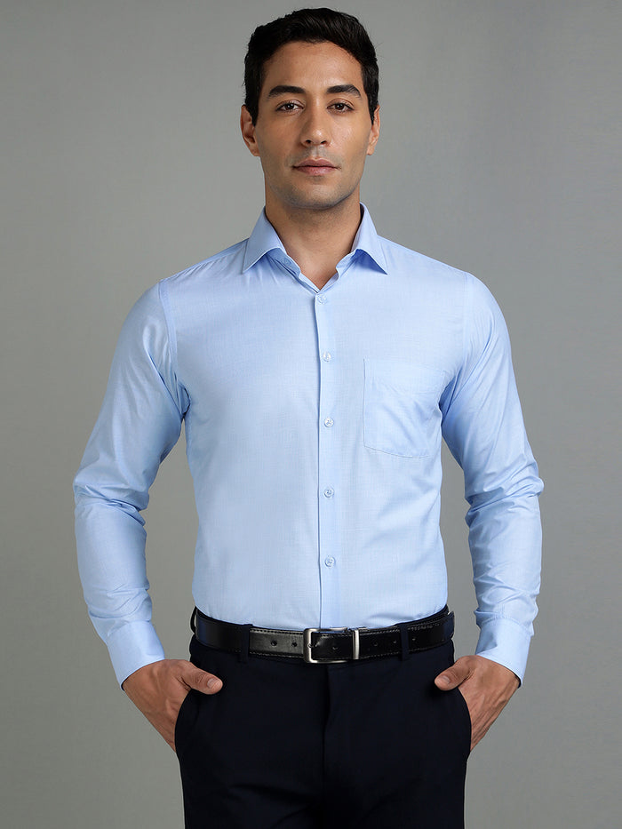Man wearing a light blue dress shirt and black pants against a gray background