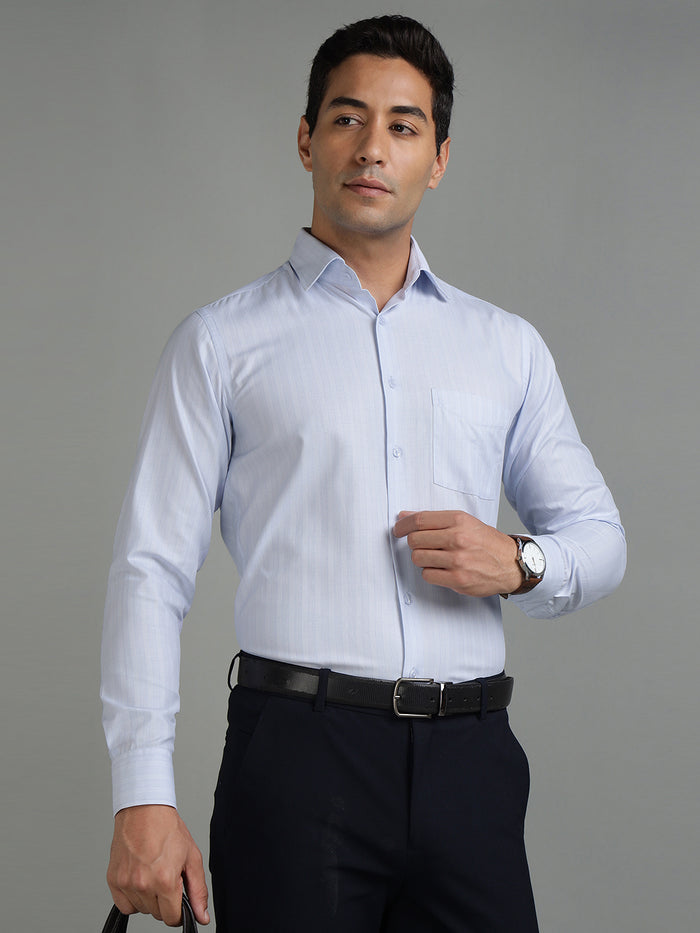 Man wearing a light blue dress shirt and dark pants against a gray background
