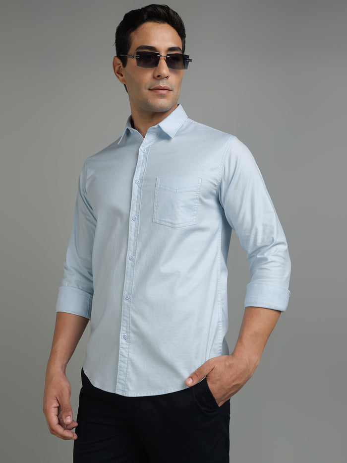 Man wearing a light blue button-up shirt with rolled-up sleeves against a gray background