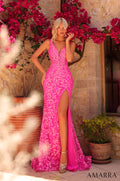 A model wears a fuchsia lace gown with a high slit, posing among red bougainvillea flowers.