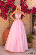 A blonde model wears an elegant, full-length light pink ball gown with lace detailing against a flowering backdrop.