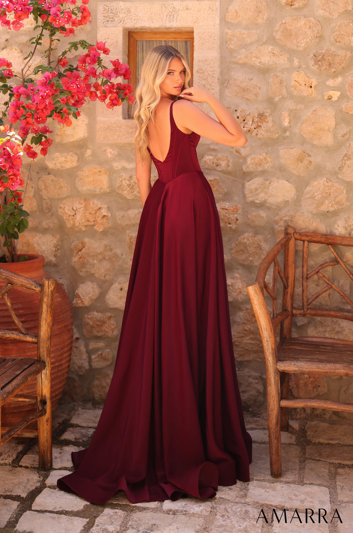 A blonde woman in a burgundy evening gown poses against a stone wall with pink bougainvillea flowers.