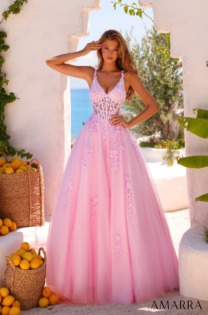A woman wears a light pink lace ball gown with floral embellishments, standing by lemon baskets near a white wall.
