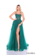 A woman wears an emerald green lace gown with a high slit and spaghetti straps, posing elegantly.