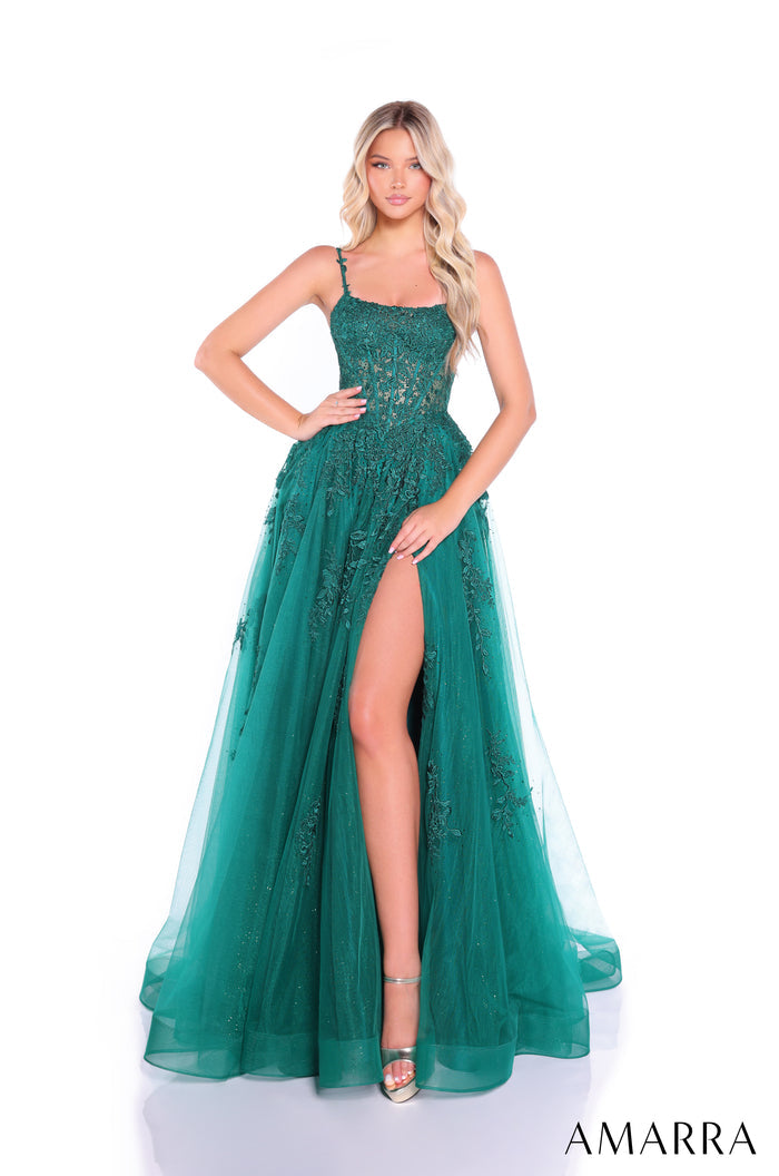 A woman wears an emerald green lace gown with a high slit and spaghetti straps, posing elegantly.